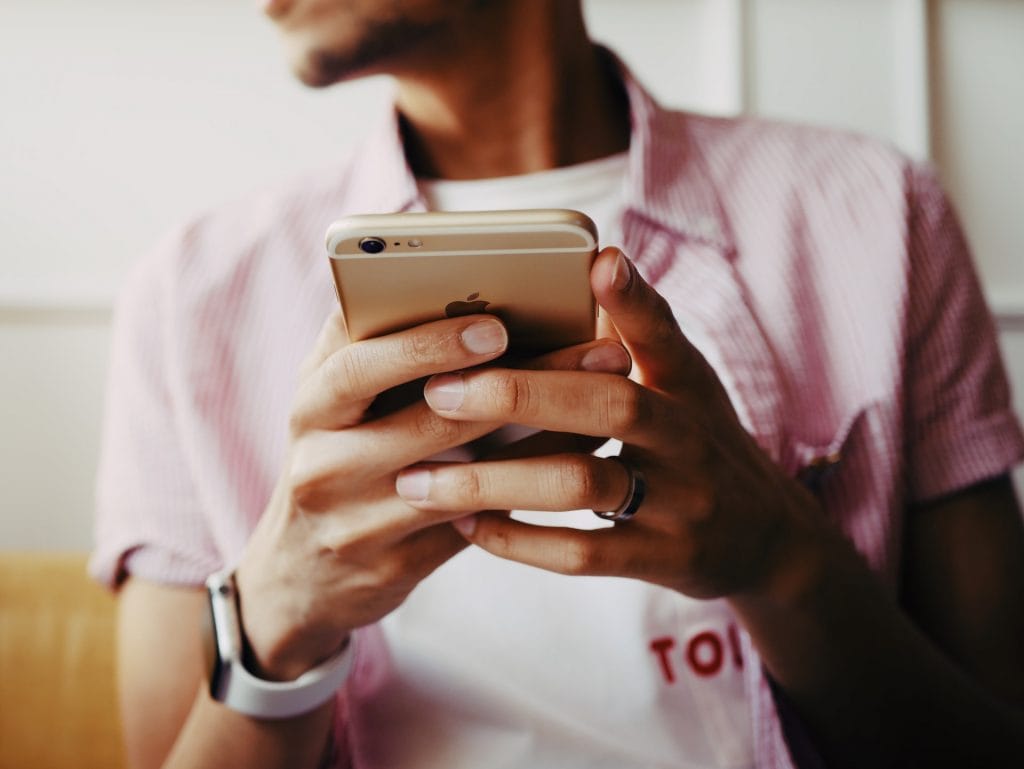 Junger Mann mit Hemd hält sein Smartphone.
