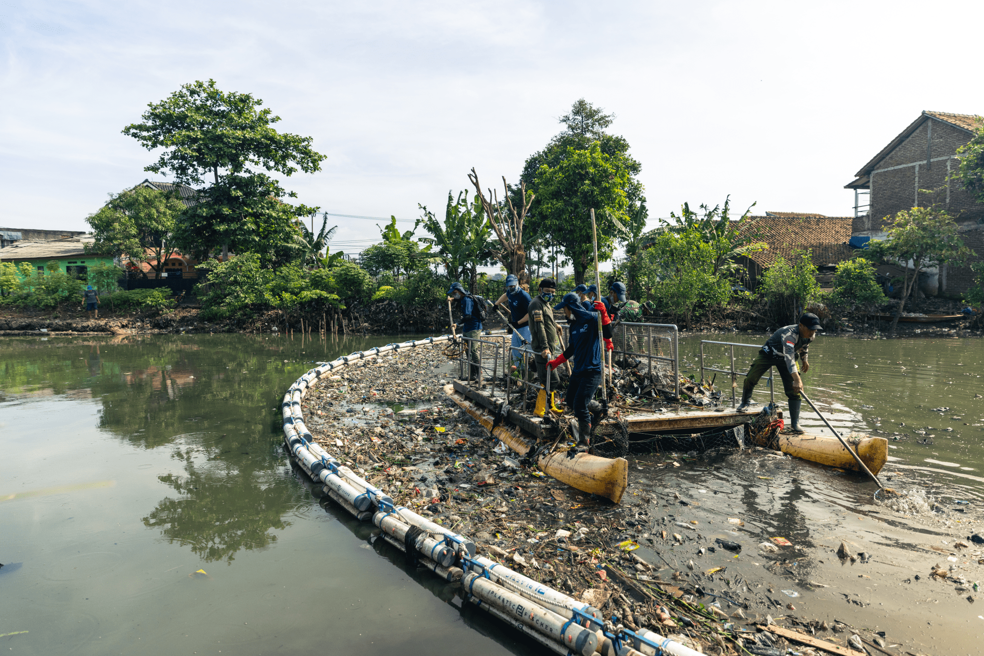 Das Bild zeigt wie eine Barriere von Plastik Fischer Müll in einem Fluss stoppt. Während auf der einen Seite das Wasser klar ist, sammelt sich der Müll auf der anderen Seite und wird dort eingesammelt