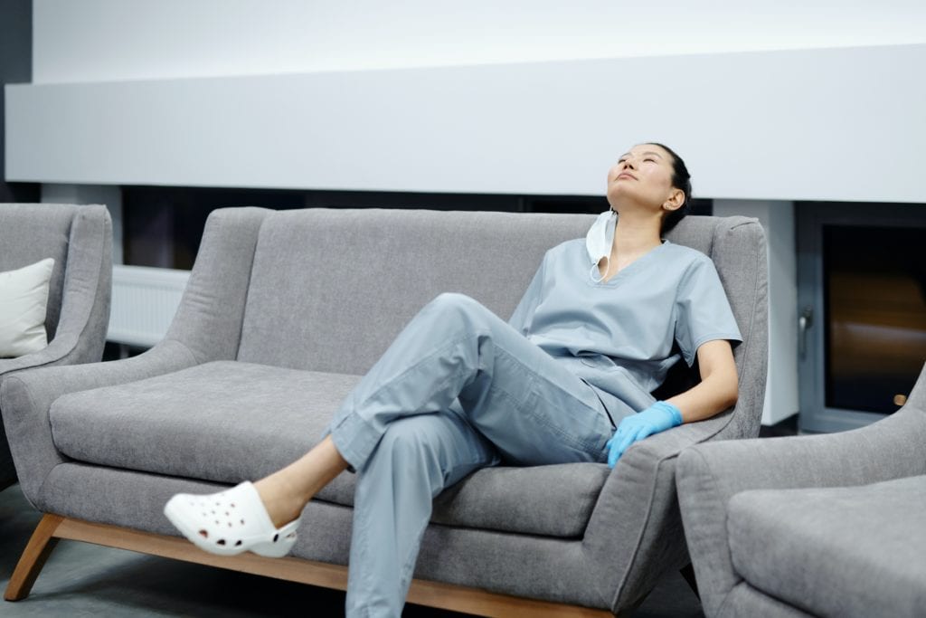 Eine Frau im Schwesternkittel sitzt müse auf einer Couch, Biorhythmus