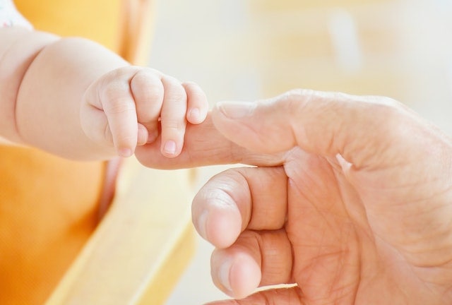 Die Hand eines Erwachsenen hält die eines Babys.