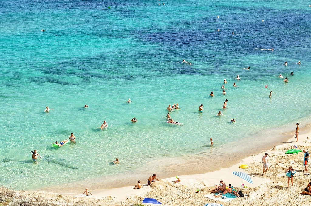 An einem Strand auf den Balearen liegen Urlauber oder schwimmen im Meer.