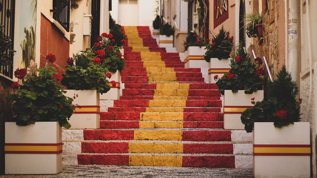 Eine Treppe ist in den Farben der spanischen Flagge angemalt und führt eine Gasse hoch.