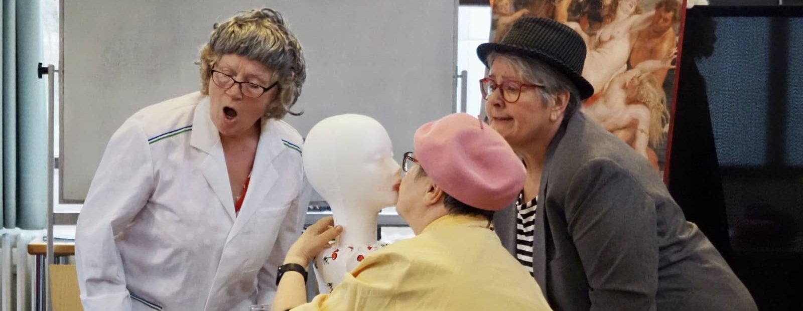 Drei Schauspielerinnen, eine von ihnen küsst einen Kopf aus Styropor