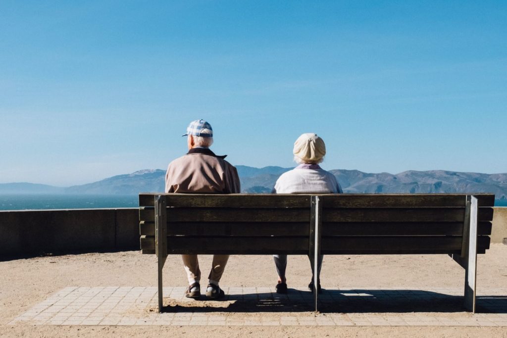 Ältere Menschen sitzen auf Bank und schauen auf ein Bergpanorama