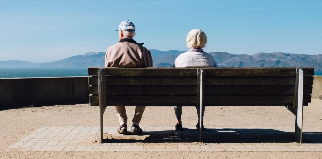 Ältere Menschen sitzen auf Bank und schauen auf ein Bergpanorama