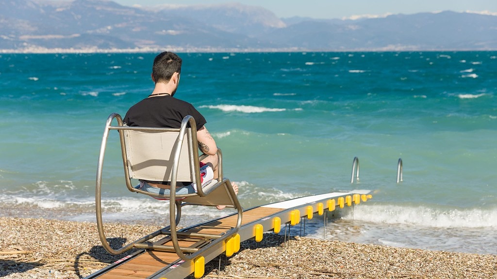 Ein Mann wird auf einem fahrbaren Sitz Richtung Meer gefahren, barrierefrei