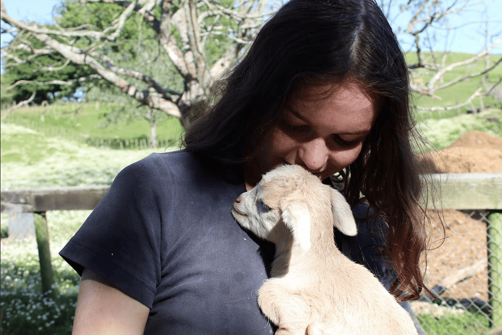 Eine junge Frau kuschelt mit einer jungen Ziege, WWOOF