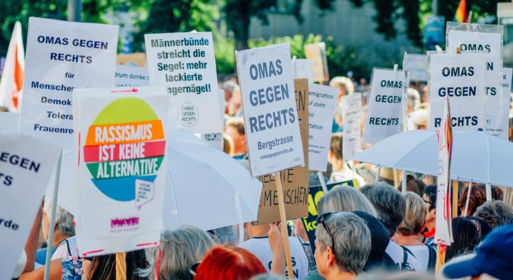 Menschen bei einer Demo und Plakate mit verschiedenen Aufschriften. Darunter mehrfach 