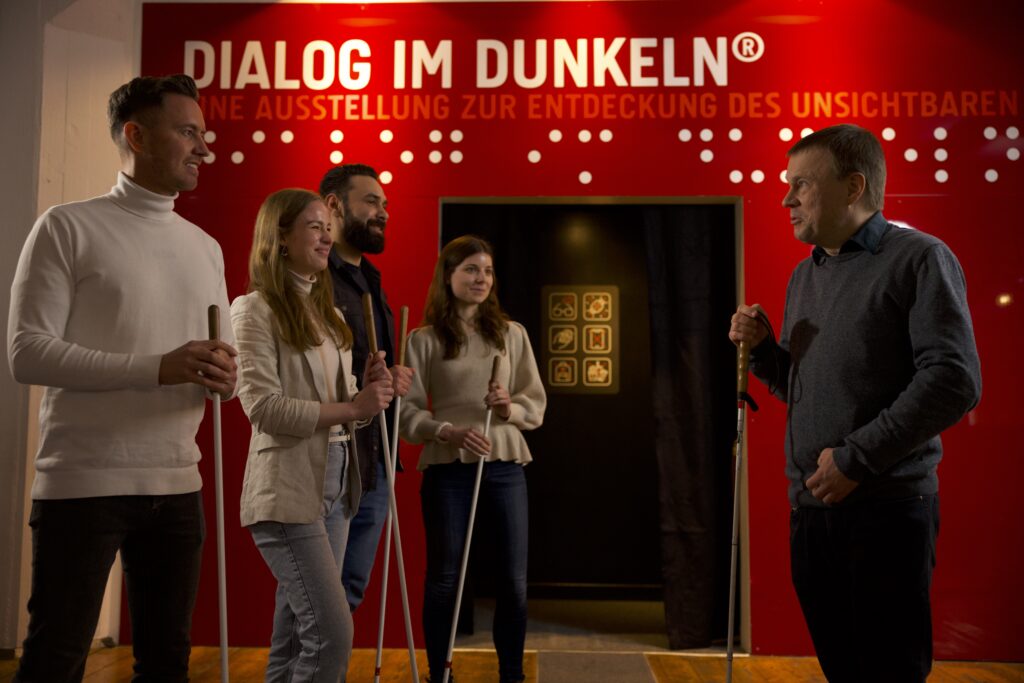 Menschen im Gespräch bei der Ausstellung "Dialog im Dunkeln". Sie halten Blindenstöcke in den Händen.